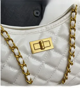 Close-up of white quilted leather texture with gold rectangular twist lock and chain strap