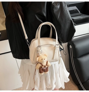 Dettaglio della borsa a secchiello bianco crema con ciondolo a forma di orsetto di peluche