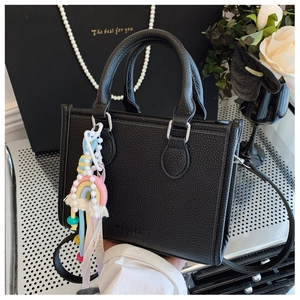 Close-up of black lychee grain leather tote bag with elegant pearl and tassel charm