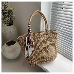 Detail of hollow woven straw tote bag featuring a brown heart print silk scarf on the handle