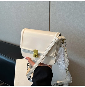 Detail of minimalist beige crossbody bag with golden twist lock and lace ribbon accent