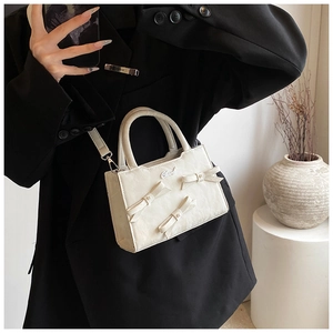Détail du sac à main blanc crème avec nœuds et logo sur une tenue blazer noir