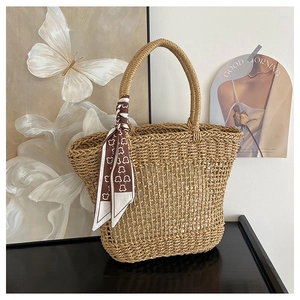 Macro detail of hollow woven straw tote bag with decorative silk scarf on the handle
