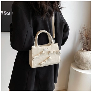 Vue détaillée du sac en cuir crème avec nœuds 3D et perles sur une veste de costume noire