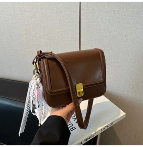 Detailed view of a brown crossbody bag with gold twist lock and delicate lace pendant