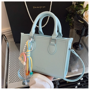 Detail of light blue lychee leather handbag with colorful rainbow charms and pearl strap