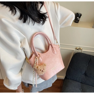 Borsa a secchiello rosa pallido con texture a pieghe e ciondolo a orsetto indossata a spalla