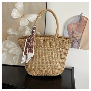 Detailed close-up of woven straw tote bag with decorative patterned silk scarf handle