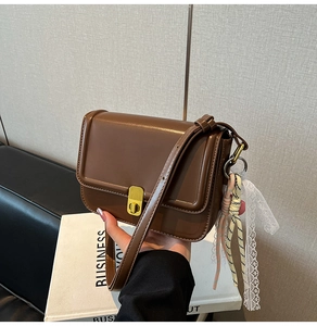 Close-up of brown crossbody bag with gold rectangle lock and decorative lace charm