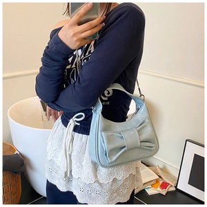 Détail du sac croissant bleu clair avec grand nœud décoratif et bandoulière en chaîne