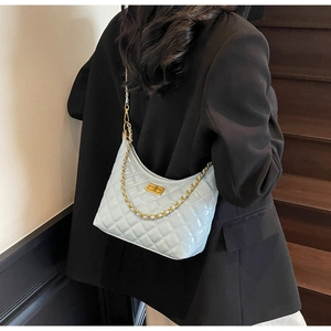 Detail of light blue quilted hobo bag with gold chain strap on model in black suit