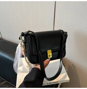 Detail of black matte crossbody bag with golden metal clasp and white lace scarf decor