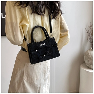 Détail du sac bandoulière noir avec trois nœuds décoratifs, perles et logo argent