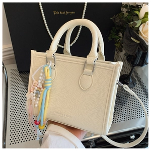 Detail of cream leather tote with lychee texture, fashion charms and detachable strap