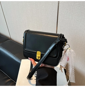 Close-up of black crossbody box bag featuring gold buckle and white lace bow detail