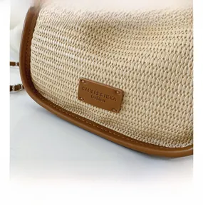 Detail of woven straw shoulder bag with brown leather trim and metallic brand plaque