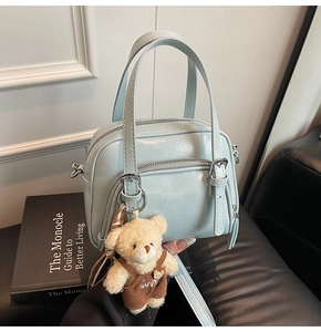 Dettaglio borsa a bauletto in pelle cerata azzurra con ciondolo a orsetto e tracolla
