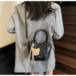 Vista posteriore di una modella con borsa a secchiello nera e ciondolo a orsetto