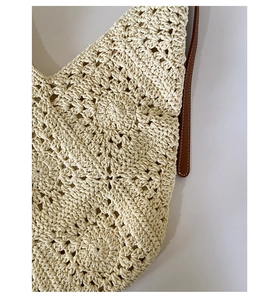 Detail of hand-crocheted floral pattern on beige beach bag with leather strap