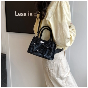 Détail d'un sac à main en cuir verni noir plissé avec nœuds décoratifs et logo en argent