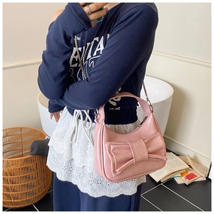 Détail d'un sac demi-lune rose avec un grand nœud et une bandoulière en chaîne