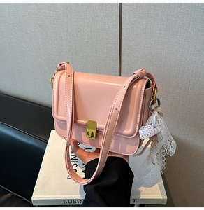 Detail of pink small square bag with glossy leather, gold clasp, and lace scarf