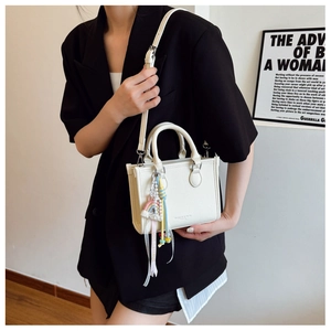 Detail of a beige structured handbag with rainbow tassel charm and slim crossbody strap