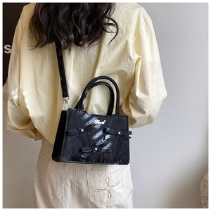 Détail du sac en cuir noir froissé orné de nœuds décoratifs et de perles blanches