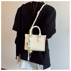 Detail of off-white lychee pattern PU leather bag with rainbow charm and lettered ribbon