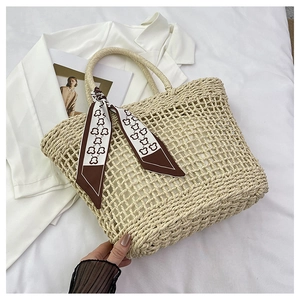 Close-up of hollow woven straw tote bag with decorative printed silk scarf on handle