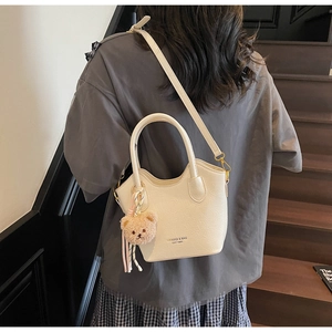 Vista esterna di una borsa a secchiello beige con un simpatico ciondolo orsetto marrone
