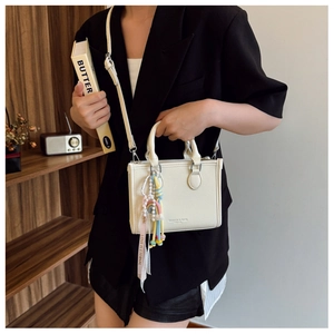 Close-up of beige crossbody bag with textured leather, pearl charm and pink ribbon strap