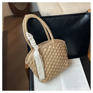Detailed close-up of a woven straw bucket bag with elegant silk scarf and pearl handle