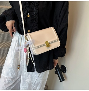 Detail of beige leather crossbody bag with golden clasp and decorative lace bow