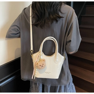 Dettaglio di una borsa a secchiello beige con trama in pelle e ciondolo a orsetto bruno