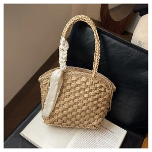 Detailed view of woven straw bucket bag featuring pearl silk scarf handle on leather chair