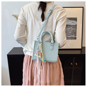 Detail of light blue pebble leather tote with colorful tassels and printed ribbon