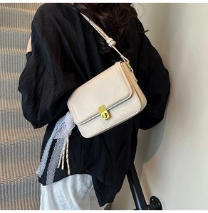 Detail of cream leather crossbody bag featuring gold twist lock and elegant lace ribbon