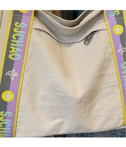 Close-up of the beige nylon tote bag featuring colorful woven shoulder straps and zipper details