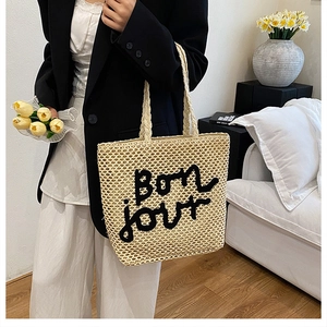 Détail d'un sac cabas en paille tissé avec broderie Bon jour noire et fleurs fraîches