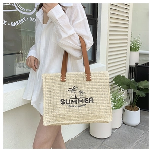 Detail of a large beige straw tote bag with palm tree print and leather handles for summer