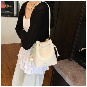 Detail of cream drawstring bucket bag featuring lychee grain texture and floral charm