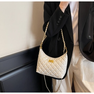 Detail of white quilted underarm bag with gold chain strap on shoulder of model