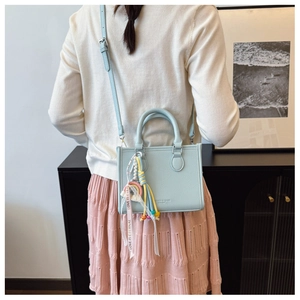 Light blue faux leather handbag with colorful tassel charm and woven strap shown on model
