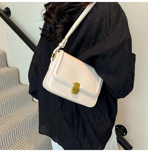 Detail of elegant cream crossbody bag with gold square buckle worn on a black shirt