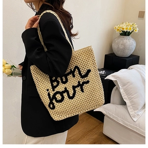 Détail de la texture tissée et du texte brodé bon jour sur le sac cabas en paille beige