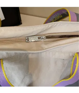 Detail of silver metal zipper puller on beige tote bag with colorful logo strap