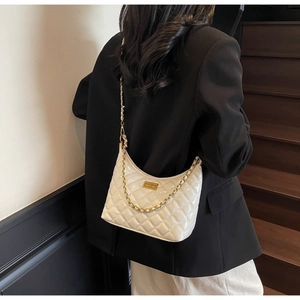 Detail of white quilted crossbody bag with golden turn-lock and chain strap on shoulder