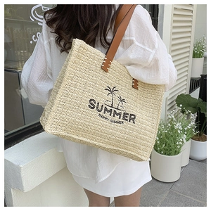 Outdoor shot of a woven straw tote bag with palm tree embroidery and brown shoulder straps