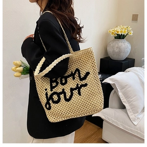 Détail d'un sac cabas en paille tressée avec lettrage bon jour noir porté à l'épaule
